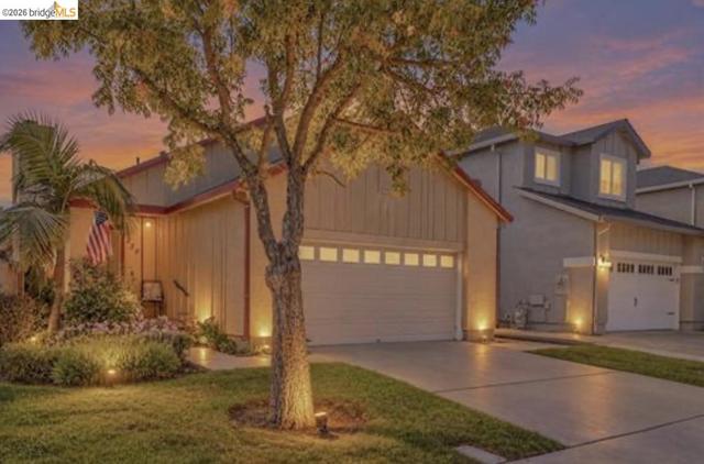 Attached two-car garage, concrete driveway, front yard landscaping, mature tree, and exterior lighting
