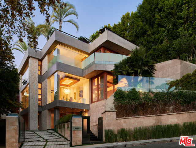 This Trophy Residence has raised the bar for Contemporary Architecture in Los Angeles. Using concrete and stainless steel this Architectural triumph features floor-to-ceiling windows, illumined waterways, mahogany walls and basalt stone. A sculptural staircase graciously leads you to the gourmet top-of-the-line chef's kitchen, a 40ft interior atrium waterfall, soaring 14ft mahogany detailed ceilings, and serene outdoor water pond. A luxurious primary suite features custom glass doors, private deck, spa like bathroom and large walk-in closet. This Estate features one of the cities best rooftop and pool to entertain your guests with views of the city and the Pacific Ocean. Landscaped private grounds and a detached guest house completes the picture. Truly a work of art, this home is a showcase for design and the contemporary Southern California lifestyle.