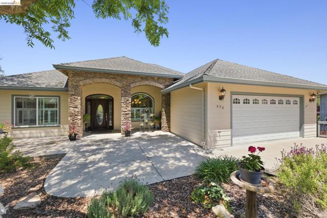 Contemporary ranch-style residence featuring a stone veneer facade, an arched entry with a decorative glass front door, a two-car garage with arched window inserts, a concrete driveway, and mature landscaping