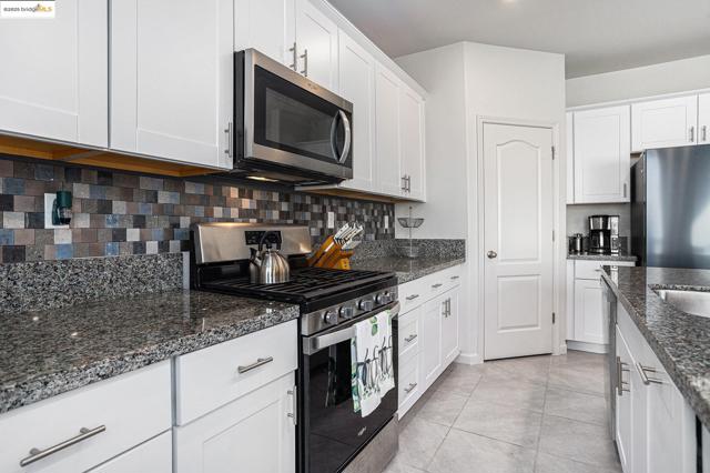 Kitchen with appliances with stainless steel finishes, white cabinetry, dark stone countertops, tasteful backsplash, and light tile patterned flooring