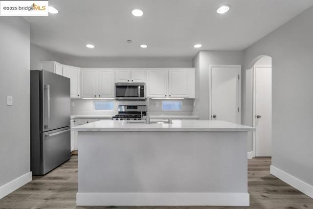 Kitchen with stainless steel appliances, white cabinetry, recessed lighting, light wood-style floors, and a kitchen island with sink