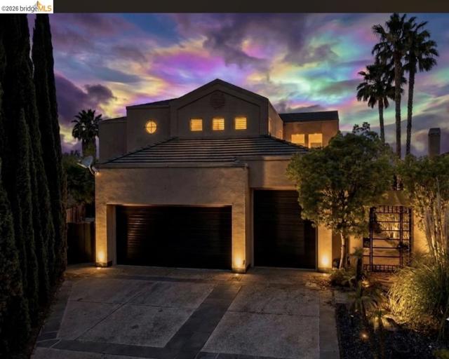 Stucco exterior architecture with a tiled roof, featuring a two-car garage, circular window detailing, and integrated landscape lighting