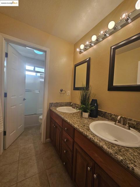 Full bathroom featuring shower / bath combination with glass door, double vanity, light tile patterned floors, and a textured ceiling