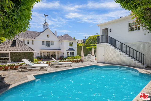1401 N Doheny Drive Los Angeles, California Perched above Sunset Boulevard, behind a private gate, is an elegant traditional estate exquisitely reimagined by top designer Tim Corrigan. An unparalleled entertainer's home with ultimate privacy and breathtaking views. Classic foyer with gleaming black and white checkered marble flooring and beautiful wrought iron staircase. Arched entry leads into the gracious formal living room with wood flooring, grand fireplace and intricately crafted coffered plaster ceiling. Well-appointed library tailor-made for book enthusiasts with beautiful custom wood paneling, a green slate fireplace, cozy bay window and built-in cabinetry. One of the greatest dining rooms in the city with a striking gold leaf ceiling, chic painted canvas walling and large windows creating a warm, bright ambiance. The breakfast room, adorned with custom French Zuber mural wallpaper, seamlessly brings the outdoors into the airy space with French doors leading out to the terrace. The gourmet chef's kitchen with adjacent butler's pantry is equipped with top-of-the-line appliances, Gorgeous powder room and maid's complete the main floor.The primary suite provides a sanctuary that captivates with large windows framing views of the verdant grounds and twinkling city lights. Lavish bathroom suite boasts a soaking tub, steam shower. Exquisite custom-designed walk-in closet fit for royalty. Three additional luxurious bedrooms suites complete the sleeping quarters, each thoughtfully designed with views. The lush private grounds, feature tranquil, open spaces. Towering hedges, a romantic vine-laden pergola, picturesque rose garden, artful latticework and refreshing swimming pool, provide an idyllic setting for alfresco dining, relaxation and lounging. Brand-new stunning guesthouse with soaring ceiling and kitchenette. 3-car garage. This extraordinary estate presents a rare opportunity to embrace an unrivaled lifestyle of beauty, privacy and serenity.