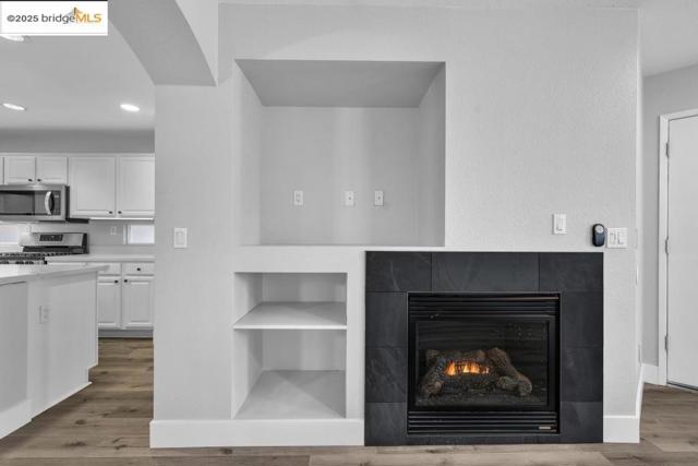 Detailed view of wood finished floors, white cabinetry, stainless steel appliances, a tile fireplace, and recessed lighting