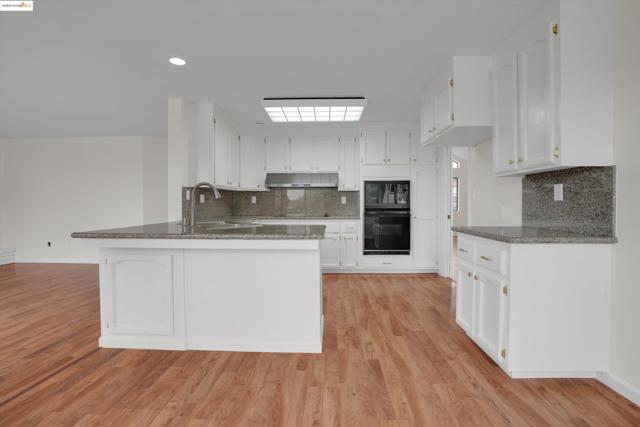 Kitchen featuring tasteful backsplash, a peninsula, dark stone countertops, white cabinets, and black appliances