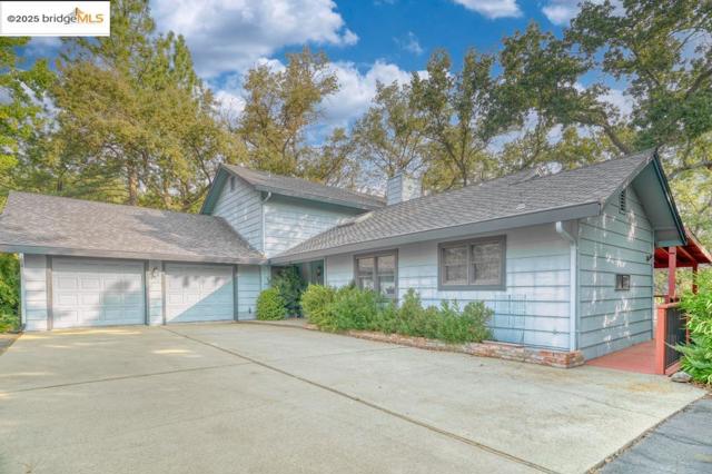 View of front facade with an attached garage, a shingled roof, concrete driveway, and a chimney