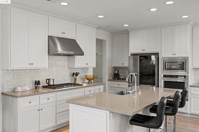 Kitchen with stainless steel appliances, decorative backsplash, under cabinet range hood, white cabinetry, and recessed lighting