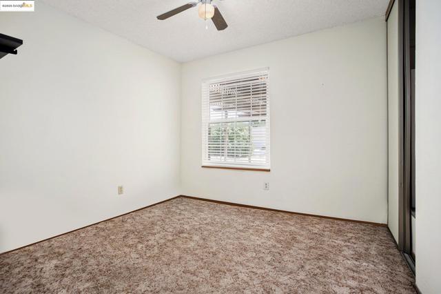 Carpeted empty room with a textured ceiling and ceiling fan