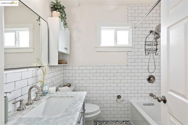 Bathroom with shower / tub combination, vanity, and tile walls