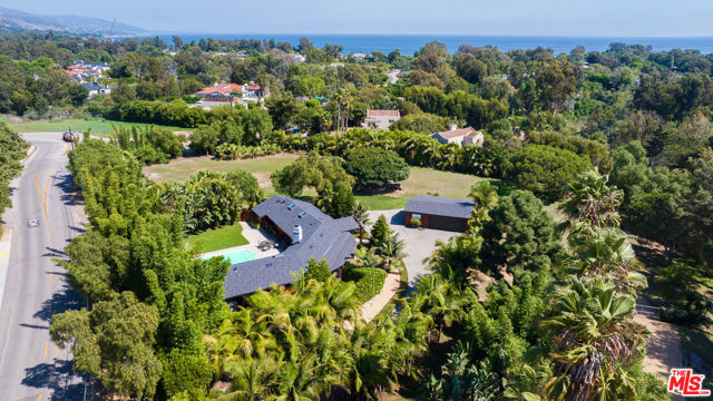 The best-priced home on Point Dume featuring the Rindge Family's historic "Rancher's Bunkhouse," exquisitely updated and remodeled to create a tropical paradise. The sale includes ~1.8 verdant acres with deeded Riviera II beach rights to Little Dume. Behind the gate lies a long driveway lined with palms, completely enclosed by fencing, mature trees, and privacy hedges. Inside, the main home offers an open-concept floor plan and high ceilings that create beautiful natural light along with recessed lighting and rich, vintage wood beams. The living room centers around a stone fireplace and features a full bar with seating and a private outdoor patio. A Chef's kitchen offers marble countertops, Viking appliances, and a large island with a wraparound breakfast bar and second sink. The primary suite is a peaceful sanctuary with sliding glass doors leading to the lush backyard, a separate enclosed patio, and a spa-like bathroom featuring a water closet, soaking tub, dual vanities, and a walk-in closet. An adjacent room offers an ideal office, den, or nursery. The comfortable guest bedroom has a vaulted wood ceiling, two closets, and an en-suite bathroom. There is an additional powder room connected to the backyard. Outside, enjoy a verdant oasis with a large pool and a massive sun-filled patio enclosed by mature trees, perfectly suited to both entertain and recharge. A detached garage offers two covered spaces, plentiful storage, and a separate gym. There is a 1 bed/1 bath guest house with a separate driveway and enclosed grounds, complete with a well-equipped kitchen, living room, and private deck with an outdoor shower and bathtub. The coveted beach rights to Little Dume provide private access to the prized sandy beach, blocked from the prevailing west wind and perfectly situated to capture south swells. This trophy property is ready to be enjoyed, expanded upon, or further developed to suit any need. The adjacent parcel is also available for sale and comes with Riviera I beach rights.