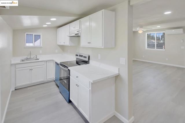 Kitchen with stainless steel appliances, light wood finished floors, white cabinetry, recessed lighting, and under cabinet range hood
