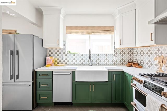 Kitchen featuring green cabinetry, appliances with stainless steel finishes, decorative backsplash, and white cabinetry