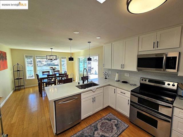Kitchen featuring stainless steel appliances, white cabinets, a peninsula, hanging light fixtures, and decorative backsplash