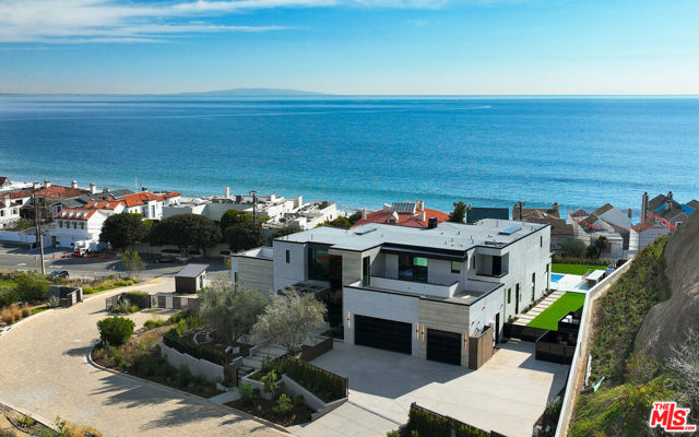Brand new and exceptionally comfortable, this handsome contemporary residence was designed by architect Doug Burdge to take full advantage of its enviable position in the gated community of Malibu Colony Estates. With a sweeping panorama that takes in the ocean, islands, and sparkling Queen's Necklace, the home's step-back design allows impressive views from almost every room. Expansive patios and decks on two levels allow vanishing walls of glass to transform rooms into open pavilions for blissful lounging, relaxed poolside gatherings, al fresco dining, and elegant entertaining. Built on three levels, all served by an elevator, the home is spacious, luminous, and designed with gracious flow for congenial living. The main floor, with high ceilings, art-gallery walls, and travertine floors, is a grand space that includes living, dining, kitchen, and family rooms, all facing onto the views through floor-to-ceiling walls of glass and opening to the generous patio and pool deck. The living room features a dramatic, modern stone chimneypiece, while the dining room and gorgeous adjacent wet bar each open to the patio when corner window walls slide away. The kitchen, which adjoins the family room, is both a cook's dream and an entertainer's hub, with stunning cabinetry, a huge island with bar seating, top-of-the-line appliances, wine storage, and a walk-in pantry. A door from the kitchen opens to the side yard, where there is a turf play area/dog run. Also on the main floor, along with two powder rooms, is an office with built-in bookshelves and a corner wall of glass pocket doors, as well as an en-suite bedroom. The central staircase, with floating treads, landing windows, and an exceptionally long pendant light fixture, ascends to the upper level, which has wood floors and is home to four bedrooms, including the primary, each with its own bath, walk-in closet, and doors opening onto an upper deck. The primary suite is truly a private sanctuary, which features corner window walls opening to a spectacular view deck with generous space for lounging; a fireplace; an all-wood walk-in closet with illuminated shelving; and two sublime en-suite bathrooms, one with glass walls that open to allow al fresco bathing. On the home's bottom floor is a large rec room with a wet bar, a full bath, a massage room, a small studio/bonus room, a powder room, and the laundry room. The ocean-view backyard, which features a zero-edge pool and Jacuzzi as well as a lawn, offers numerous open and covered seating options, including a sunken fire pit, and a built-in Kalamazoo barbecue area with bar seating. Along with smart-home technology for comfort and security, the home has a three-car garage plus parking for ten additional vehicles in the driveway. Set behind gates on over 1.3 acres, this compelling architectural residence is open, private, and timeless.