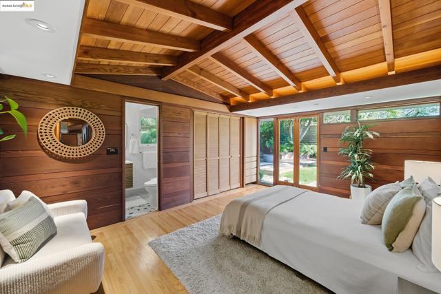 Bedroom with wooden walls, access to outside, light wood-type flooring, connected bathroom, and wood ceiling