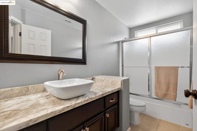 Full bath with a textured wall, enclosed tub / shower combo, vanity, light tile patterned floors, and a textured ceiling