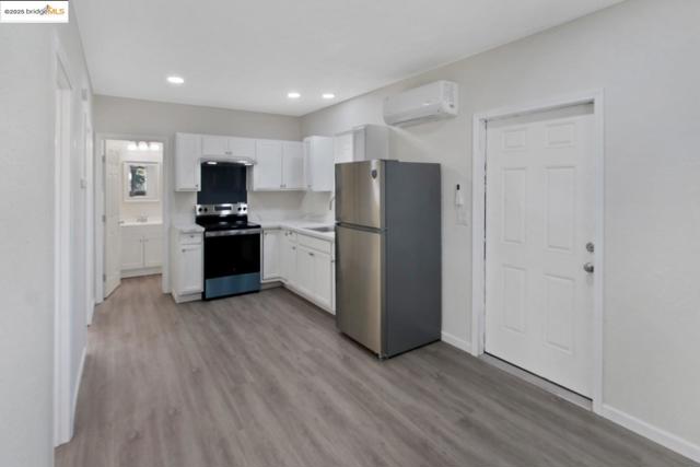 Kitchen featuring appliances with stainless steel finishes, white cabinetry, light countertops, light wood-style floors, and a wall mounted air conditioner