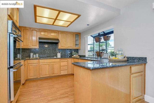 Kitchen featuring a peninsula, backsplash, dark stone counters, light wood finished floors, and light brown cabinets