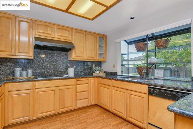 Kitchen with dishwasher, tasteful backsplash, dark stone counters, and light wood-style flooring