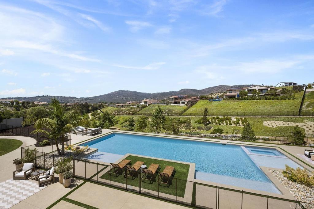 Experience the pinnacle of luxury living in one of San Diego’s most coveted neighborhoods. Welcome to this breathtaking Sterling Heights 1X Estate, nestled within the prestigious gated community of The Lakes Above Rancho Santa Fe. With awe-inspiring views and high-end finishes throughout, this exceptional property offers a spacious backyard oasis complete with a resort-style pool, spa, built-in BBQ, and cozy fire pit—perfect for both relaxation and entertaining. Set on a premium view lot just shy of 1 acre, this 5-bedroom, 5.5-bath estate spans 4,936 sq. ft. and blends sophistication, comfort, and functionality. Soaring 22-foot ceilings make a grand first impression, while expansive windows and a retractable glass wall flood the home with natural light and create seamless indoor-outdoor flow. The formal dining room and chef’s kitchen—featuring sleek white cabinetry and top-tier appliances—are ideal for both everyday living and hosting gatherings. The highly desirable 1X floor plan includes four generously sized en suite bedrooms on the main level, offering comfort and privacy for family and guests. Upstairs, a fifth bedroom with a full bath and access to a large private terrace provides a peaceful retreat. The primary suite overlooks the backyard and features a spa-inspired bath with dual vanities, a soaking tub, and a spacious walk-in shower. A large upstairs loft adds versatile space for a media room, play area, or additional lounge. Located within the prestigious Poway Unified School District, The Lakes Above Rancho Santa Fe offers a family-friendly community and an unbeatable Southern California lifestyle. Del Norte High, a top-rated school, is just a stone's throw away. Within half a mile, residents can also enjoy optional club memberships and world-class amenities at The Crosby Club at Rancho Santa Fe, including golf, dining, entertainment, a fitness center, tennis, pickle ball, and a heated lap pool. With an array of 25 golf courses, 17 parks, and 4 hiking reserves within a 10-mile radius, as well as over 79 restaurants within 5 miles, there is no shortage of activities to relish. Conveniently located minutes from the I-15 and CA-56 freeways, this exceptional property offers unparalleled access to all that San Diego has to offer. Don't miss this extraordinary opportunity to own the exquisite Sterling Heights estate and embrace the ultimate California dream.