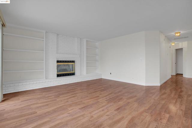 Unfurnished living room with light wood finished floors, built in features, and a fireplace