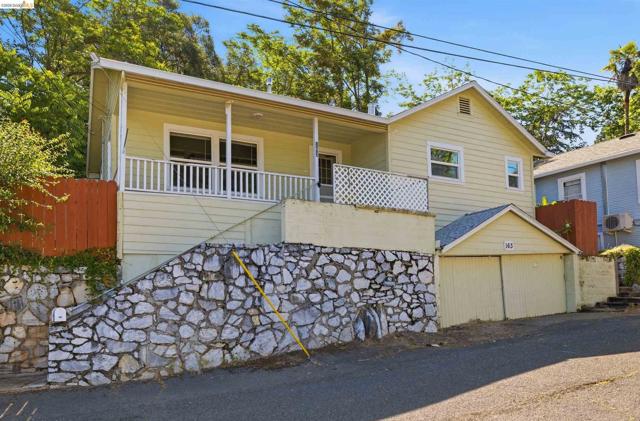Exterior featuring light yellow siding, white porch railings, a full-width covered porch, and a stone retaining wall