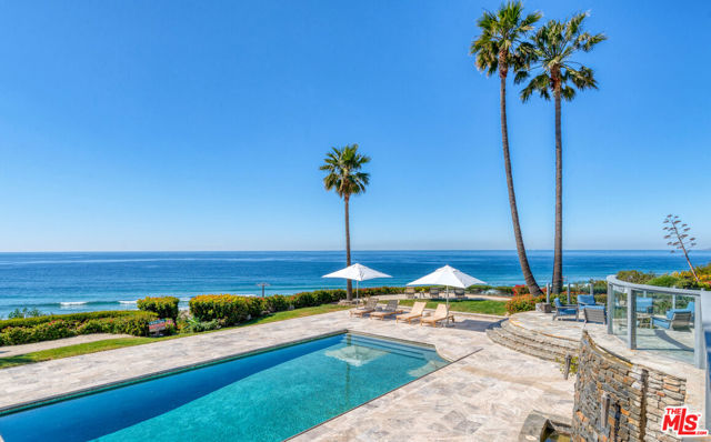 Breathtaking ocean views, an expansive and idyllic garden setting, and exquisite amenities inside and out add up to a majestic resort-style compound of unmatched quality and beauty, with approximately 208 feet of bluff frontage. Set behind gates at the end of a tree-lined drive, this exceedingly private estate commands 180-degree vistas from its two-acre bluff above Zuma Beach. Befitting an indoor-outdoor lifestyle of lavish entertaining and undisturbed sanctuary, the home is light-filled and open, with high ceilings, walls of glass, and brand-new hardwood floors throughout. The centerpiece of the main floor is the huge living/dining great room, with a fireplace, gorgeous ocean views and a patio just outside. Two steps up is a separate dining room and the stunning chef's kitchen, with generous counter and cabinet space, a large island, bar seating, top-quality appliances, a butler's pantry, and, of course, ocean views. Beyond the kitchen is a powder room and an en-suite bedroom. On the upper floor, in addition to the spacious primary suite with chandelier ceilings, ocean view balcony, and spa-style bath, there are three en-suite bedrooms, an ocean-view office/bedroom, powder room, laundry room, and a grand office/media room with coffered ceiling, lustrous wood paneling, ocean views and a balcony just outside. Stairs from an upper-level balcony lead to a lovely rooftop patio with crow's-nest sunrise-to-sunset views. At the end of the upper hallway, stairs lead down to the gym, which could also be set up as an elegant guest suite, with very high ceilings, wraparound windows, en-suite bath, and sets of French doors opening to a flagstone deck where a Jacuzzi overlooks the pool and views. Below the gym is a huge bonus/recreation room with flagstone floors, plus a powder room and a Deco-style movie theater with a kitchenette. The property has expansive outdoor areas at the front and the back of the house. At the front, along with manicured lawns and magnificent mature trees, there is a large sport court, a studio shed, a tranquil pond and waterfall, and a relaxing patio set among beautiful plantings. The resort-like backyard, surrounding the Pebble Tec pool, is a magical collection of enchanting areas designed for dining, lounging, recreation, entertaining, and simply enjoying the non-stop panorama of sky, sea, and shoreline. Features include a large fire pit with seating, an outdoor kitchen/barbecue area, a private sandy beach-like vista point, stone fountains with torches, manicured lawns, and towering palms wrapped with sparkling lights. Unrivaled in quality and setting, this remarkable estate is spacious, harmonious and uncommonly beautiful.
