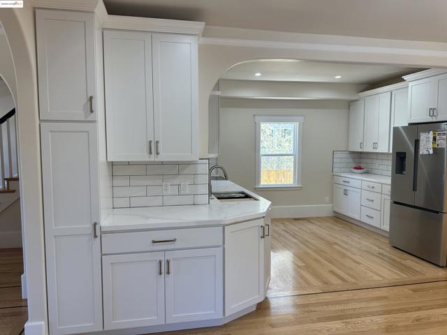Kitchen with stainless steel fridge, tasteful backsplash, arched walkways, light wood-type flooring, and white cabinets