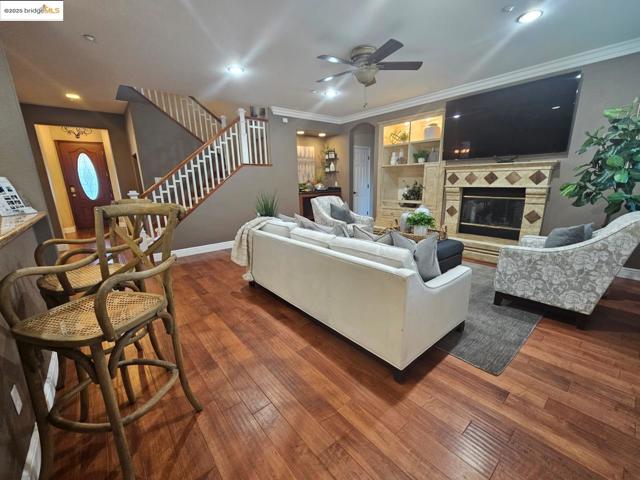 Living room featuring stairs, arched walkways, dark wood-type flooring, a tiled fireplace, and crown molding
