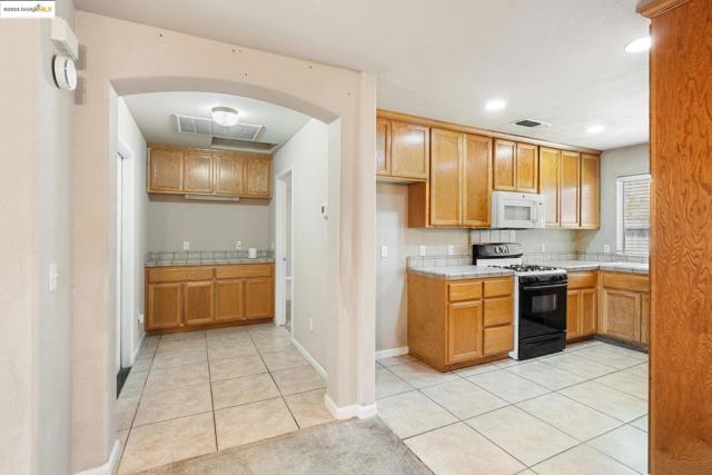 Kitchen featuring light tile patterned floors, gas range oven, tile counters, recessed lighting, and white microwave