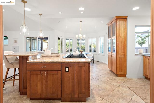 Kitchen with brown cabinetry, decorative light fixtures, a chandelier, glass insert cabinets, and a breakfast bar