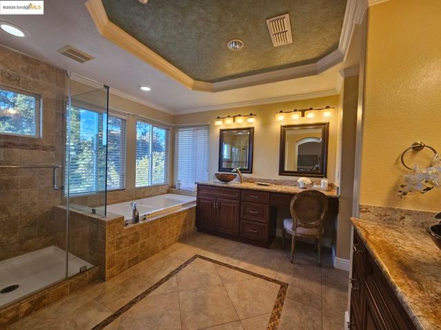Full bathroom with ornamental molding, inlaid floor details, vanity, a garden tub, and a raised ceiling