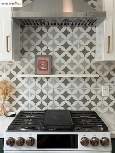 Kitchen view of wall chimney range hood, white cabinets, white range with gas cooktop, and decorative backsplash