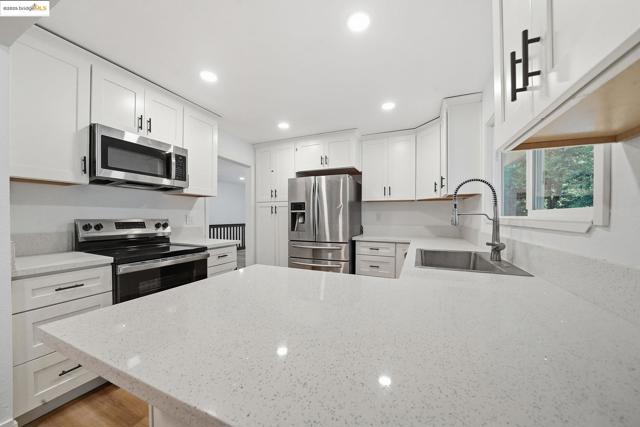 Kitchen with light stone countertops, appliances with stainless steel finishes, a peninsula, white cabinets, and recessed lighting