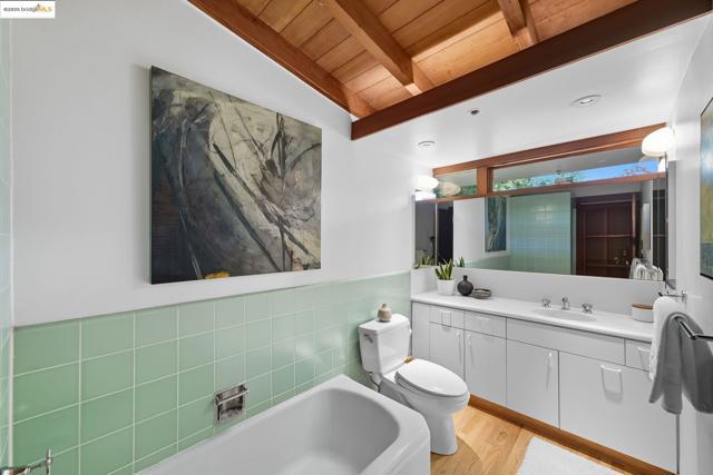 Full bath with tile walls, vanity, light wood-style flooring, a garden tub, and wainscoting