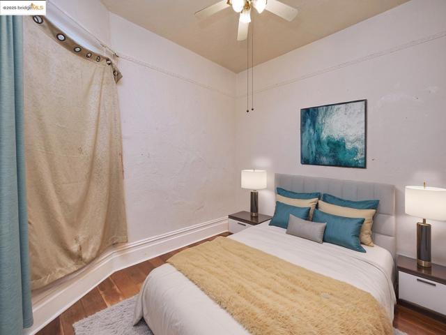 Bedroom with wood-type flooring, a ceiling fan, and a textured wall. Virtually staged.