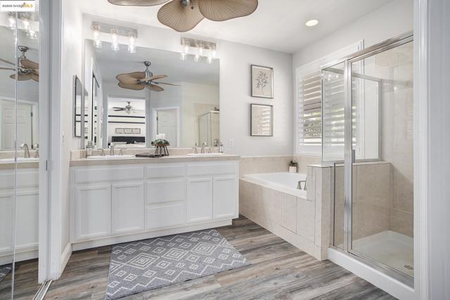 Bathroom with a bath, a shower stall, double vanity, laminate wood finished floors, and recessed lighting