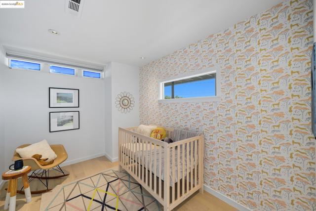 Bedroom with wallpapered walls, a nursery area, light wood-style floors, and recessed lighting