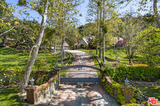 This magical estate compound is unlike any property in Westlake Village. Unique in so many ways - it's charm, acreage, privacy, grounds, sustainability and clean living. Enter a private gated driveway past the pond and bridge to the enchanting home canopied by mature oaks and sycamores. Completely reimagined from head to toe, this single-story home is like a true storybook. All four bedrooms in the main house are en-suite - each with its own view of the verdant grounds or access to the beautiful backyard. An enormous wood-burning fireplace is the focal point of the family room with beamed vaulted ceilings that is open to the kitchen as well as another sitting room/game room. The home also has formal elements such as a separate dining room, open living room and two separate powder rooms. The grounds are exceptional - easily maintained through an on-site well which translates to no water bill! Rolling lawns, a beautiful pool with spa and cascading waterfall, hidden pathways and organic orchard and vineyard with over 600 organic fruit trees. The main house is accompanied by a detached two bedroom fully equipped guest house with its own address, plus a separate structure with 4 car garage. No need to leave the property to enjoy several meandering pathways that lead you to the copious variety of fruit trees, special nooks and sitting areas. Sustainable living with impeccable style!