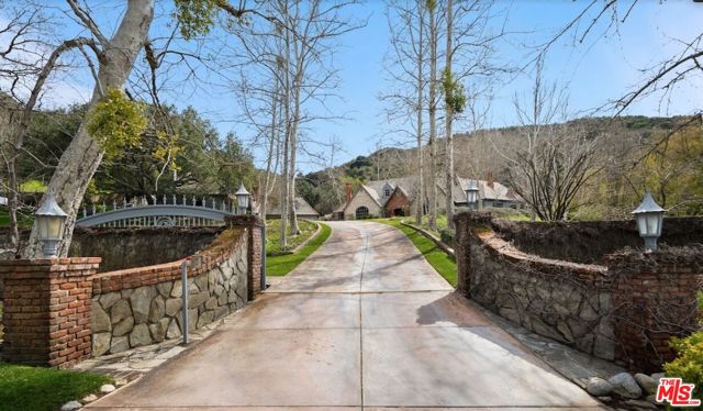 This magical estate compound is unlike any property in Westlake Village. Unique in so many ways - it's charm, acreage, privacy, and grounds. Enter a private gated driveway past the pond and bridge to the enchanting home canopied by mature oaks and sycamores. Completely reimagined from head to toe, this single-story home is like a true storybook. All four bedrooms in the main house are en-suite - each with its own view of the verdant grounds or access to the beautiful backyard. An enormous wood-burning fireplace is the focal point of the family room with beamed vaulted ceilings that is open to the kitchen as well as another sitting room/game room. The home also has formal elements such as a separate dining room and open living room. The grounds are exceptional. Rolling lawns, a beautiful pool with spa and cascading waterfall, hidden pathways and organic orchard and vineyard. The main house is accompanied by a detached two bedroom fully equipped guest house with its own address, plus a separate structure with 4 car garage. No need to leave the property to enjoy several meandering pathways that lead you to the copious variety of fruit trees, special nooks and sitting areas. Feels like another world, but you're only 4 minutes from the heart of Westlake!