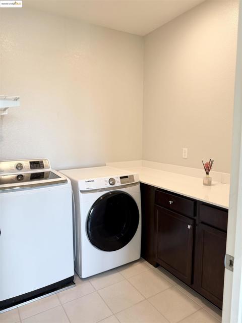 Laundry area featuring light tile patterned floors, washing machine and clothes dryer, and cabinet space