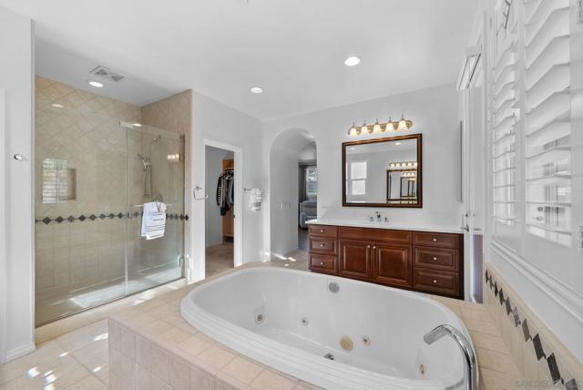 Primary suite spa bathroom with double sinks, oversized bath tub, walk in shower, and two walk in closets. two doors leading out to covered outdoor patio overlooking the gorgeous back yard and pool with mountain views.