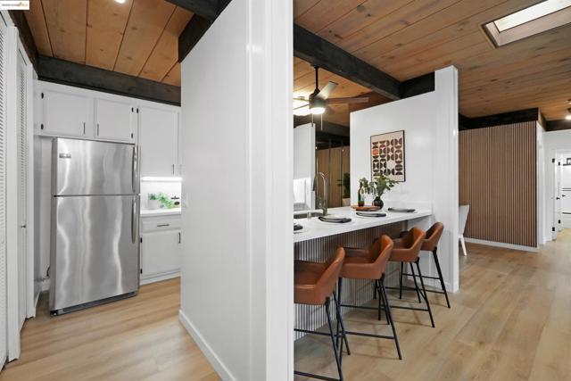 Kitchen featuring a wood ceiling with exposed beams, white cabinets, freestanding refrigerator, light wood-style flooring, and a breakfast bar