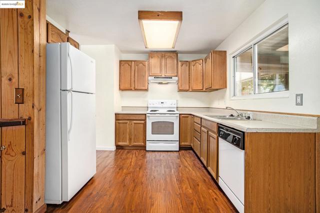 Kitchen with light countertops, white appliances, dark wood-style flooring, brown cabinetry, and under cabinet range hood