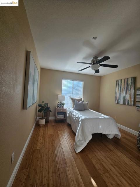 Bedroom featuring wood-type flooring, a ceiling fan, and a textured wall