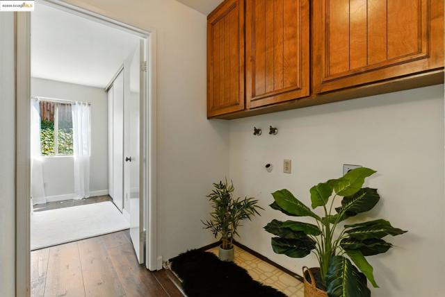 Washroom with electric dryer hookup, dark wood finished floors, and cabinet space
