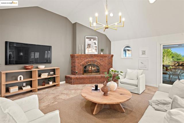 Living area featuring lofted ceiling, a brick fireplace, and a chandelier