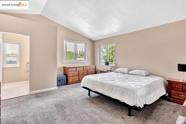 Bedroom with a textured wall, light colored carpet, and lofted ceiling
