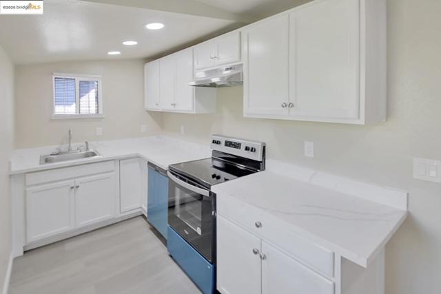 Kitchen featuring appliances with stainless steel finishes, white cabinetry, under cabinet range hood, recessed lighting, and light wood finished floors